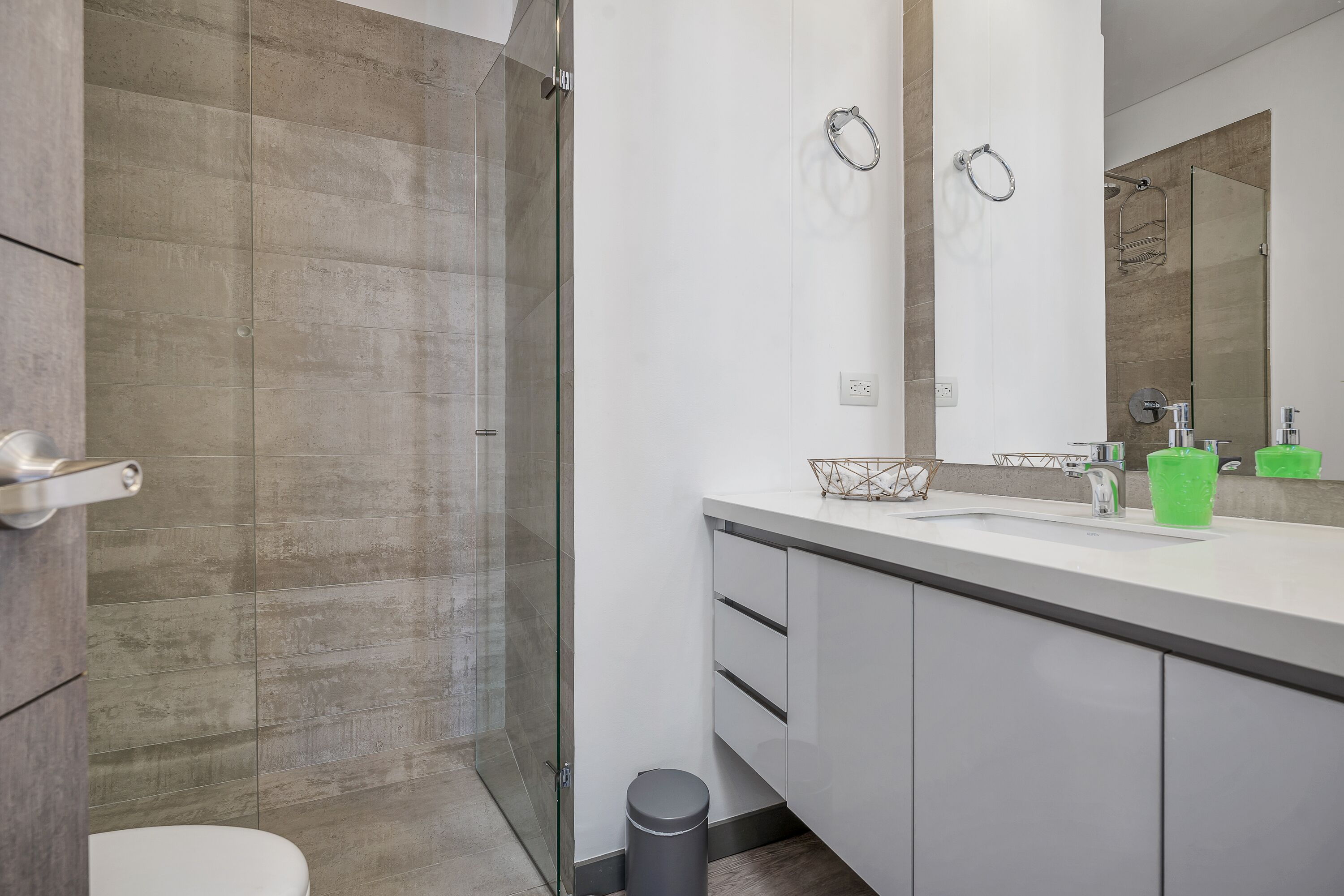 A modern bathroom with a glass shower enclosure, a white sink with a mirror above it, and a toilet.