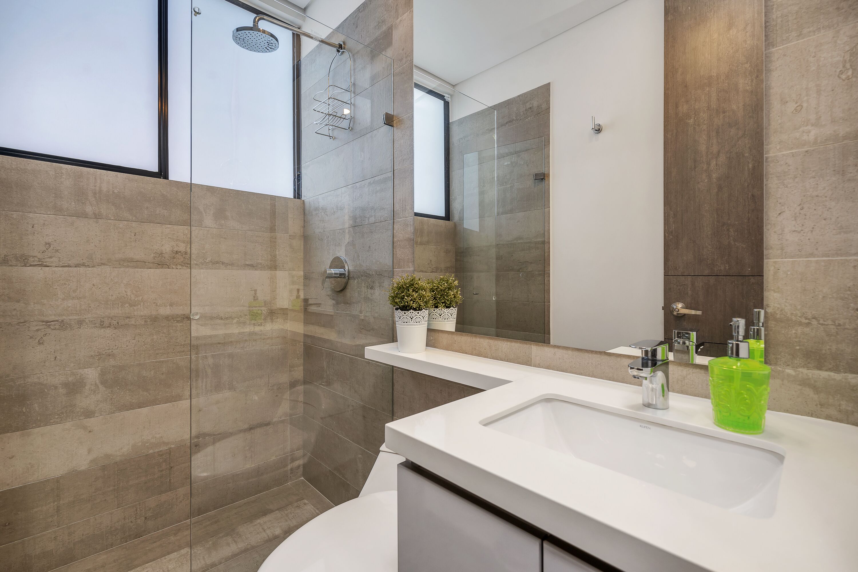 A modern bathroom with a glass shower enclosure, a white vanity with a large sink, and a mirror above the vanity.