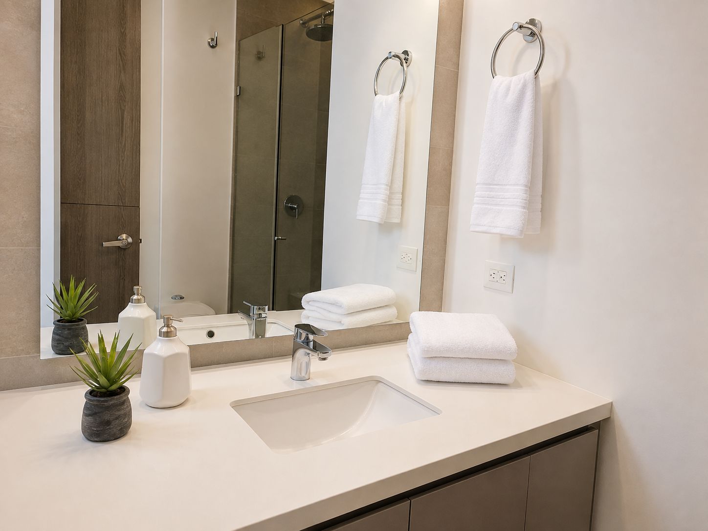 Un baño moderno con un espejo grande, un lavamanos, dos toallas y una planta en maceta.