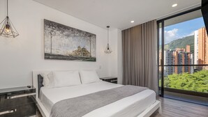 Quarto moderno com uma cama grande, mesa de cabeceira, pintura e vista para edifícios e áreas verdes.