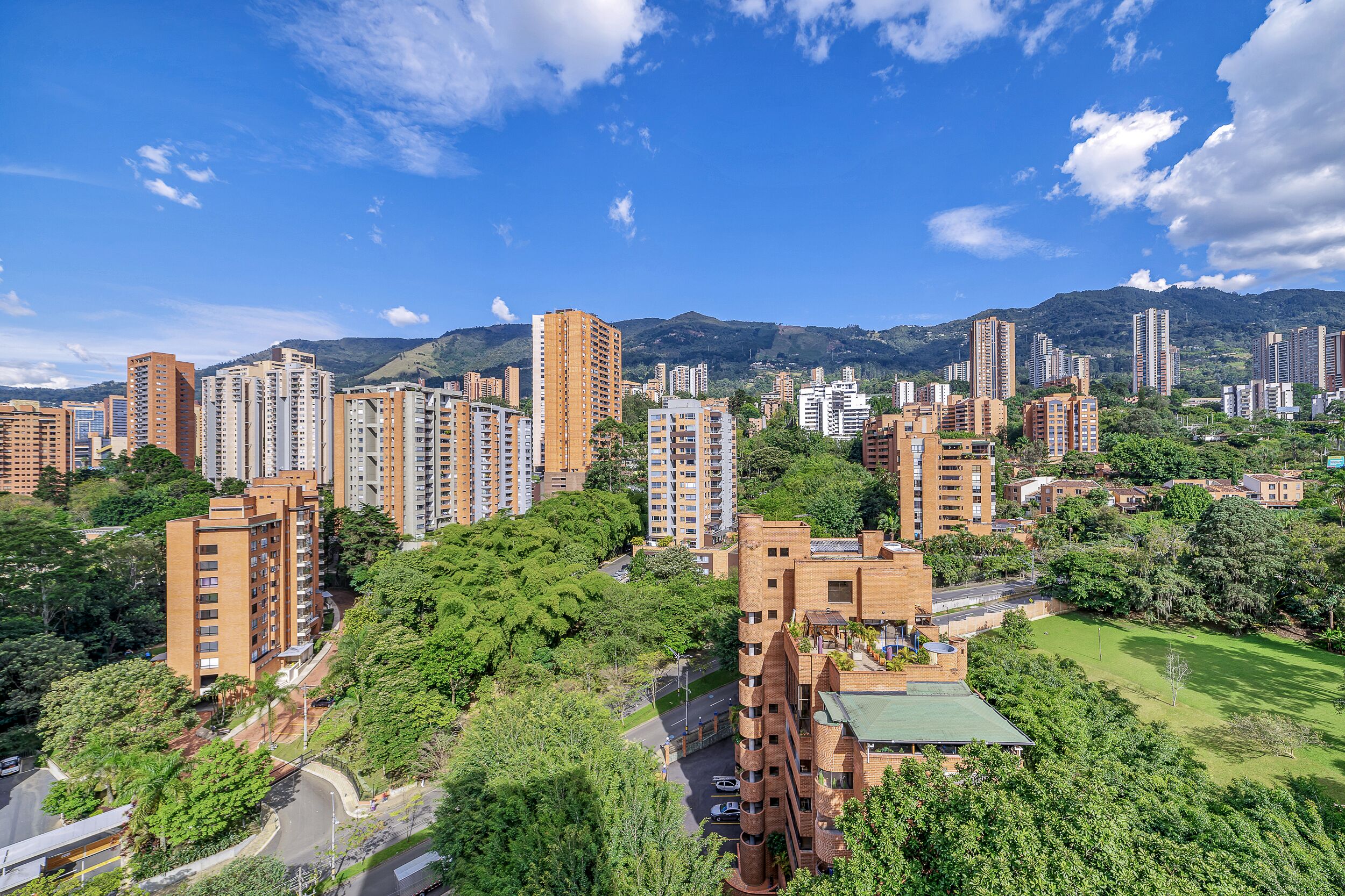 Un ensemble immobilier résidentiel composé de plusieurs immeubles à étages, entouré de verdure et avec des collines en arrière-plan.