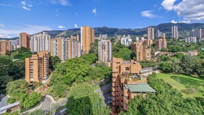 Ett högt bostadskomplex med flera bostadshus, omgivet av grönska och kullar i bakgrunden.