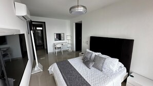 Habitación de hotel moderna con una cama grande, un escritorio, una silla, un televisor y un armario.