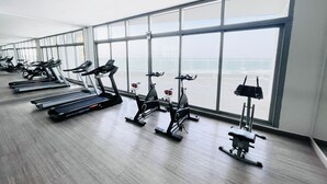 Un gimnasio con cintas de correr, bicicletas estáticas y elípticas alineadas, con grandes ventanales que ofrecen vista al océano.