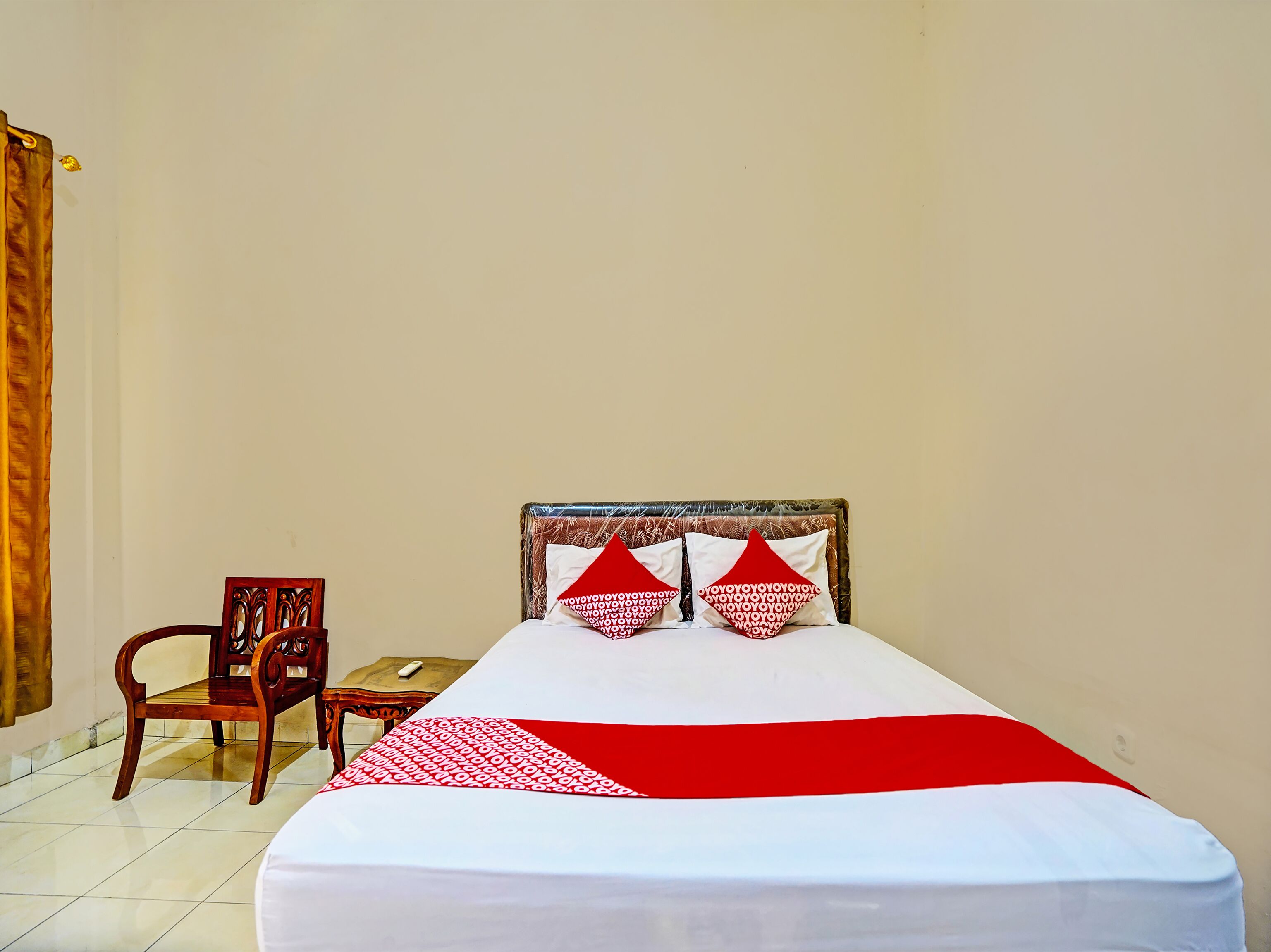 Un lit simple avec une couvre-lit blanche et rouge, deux oreillers rouges ornés de motifs blancs, une chaise en bois et une petite table.