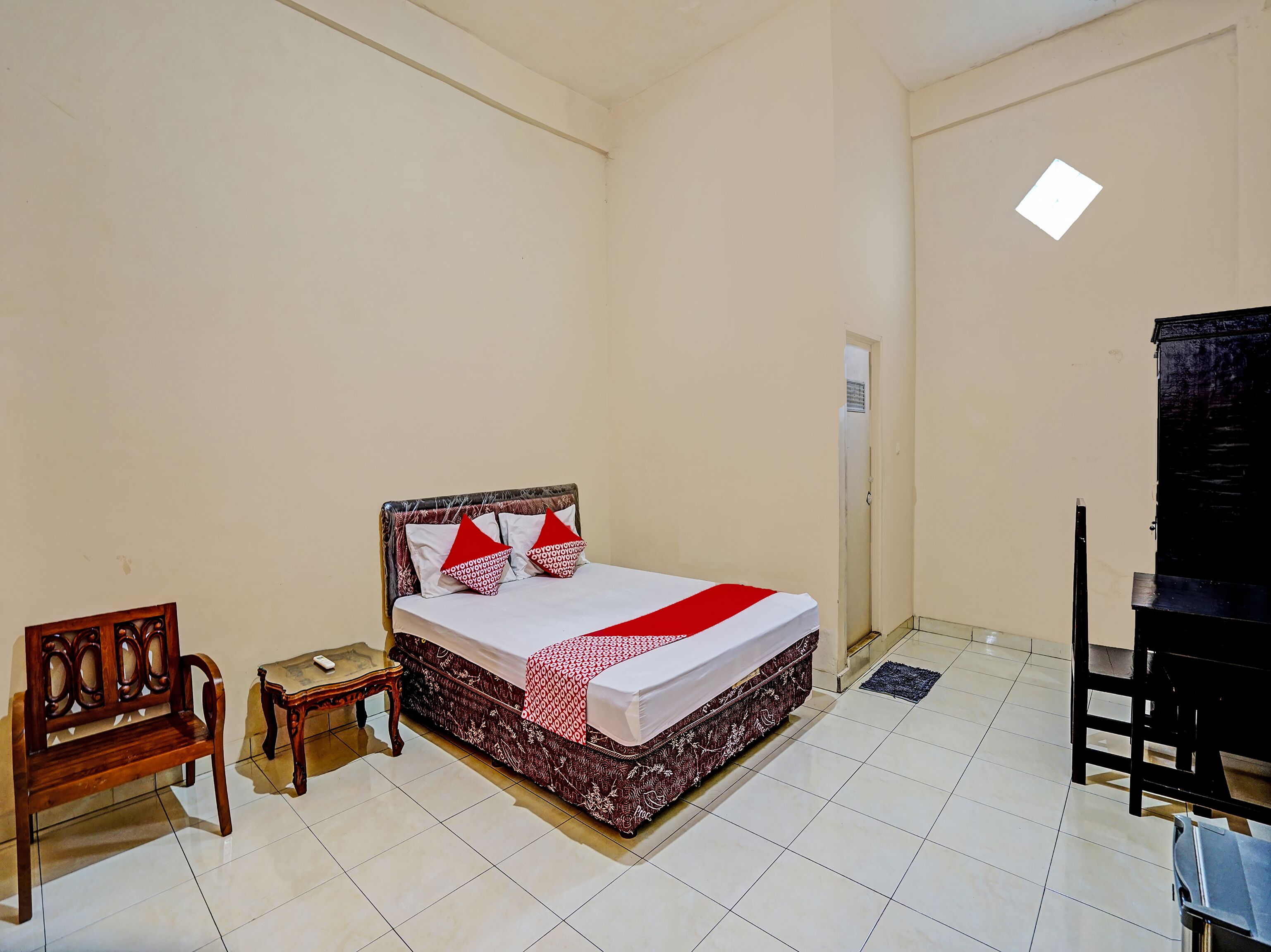 A bedroom with a bed, a wooden bench, a small table, and a black cabinet.