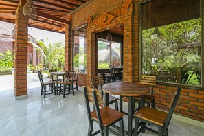An outdoor cafe with brick walls, large windows, and wooden furniture. - SPOT ON 90882 Sari Homestay Near Garuda Wisnu Kencana (Ungasan)