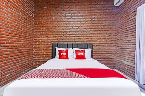 A room with a brick wall, a bed with white bedding and red pillows, and a red and white patterned throw. - SPOT ON 90882 Sari Homestay Near Garuda Wisnu Kencana (Ungasan)