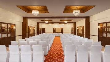 A conference room with rows of white chairs, wooden paneling, and chandeliers.