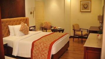 A hotel room with a large bed, a small round table with a fruit bowl, a chair, and a desk with a vase.