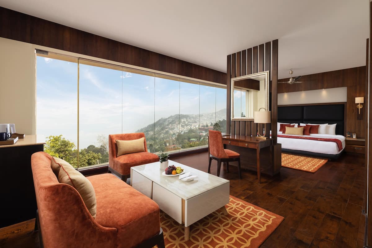 A modern hotel room with a large window, a sofa, a desk, a bed, and a ceiling fan.