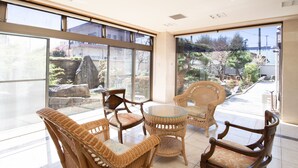 Una habitación con muebles de mimbre, una mesa de cristal y vistas a un jardín a través de amplios ventanales.