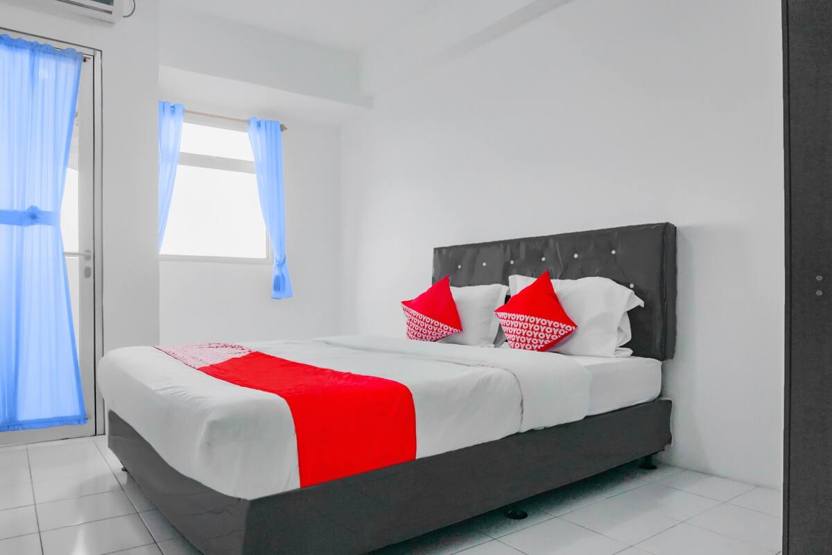 A neatly made bed with white and red bedding, a grey headboard, and two red pillows.