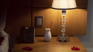 Uma mesa de cabeceira com abajur, vaso e telefone.