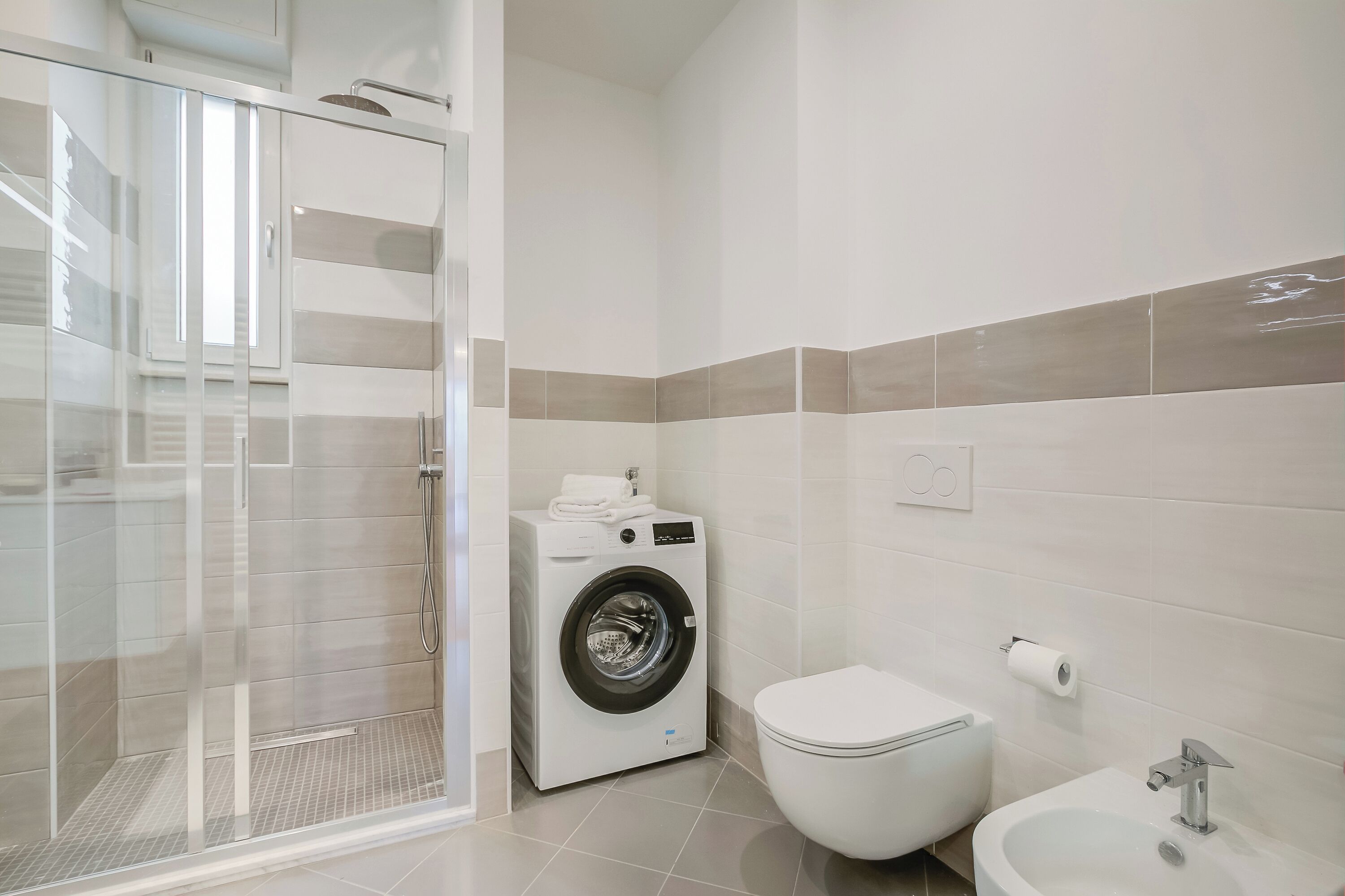A modern bathroom with a glass-enclosed shower, a front-loading washing machine, a toilet, and a sink.