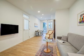 A modern living room with a flat-screen TV, a grey sofa, a patterned rug, and a dining area in the background.