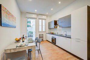 A modern kitchen with white cabinets, a dining area with a table set for two, and a window providing natural light.