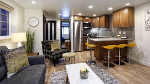 A modern kitchen with wooden cabinets, a stainless steel refrigerator, and a microwave. There is a dining area with a table and chairs, and a living room with a sofa and a lamp. - One Block to Aspen Mtn, Dining, Shops & Nightlife. AC In Bedroom! W/D, Gas FP, Pool, HT, Parking (Aspen)