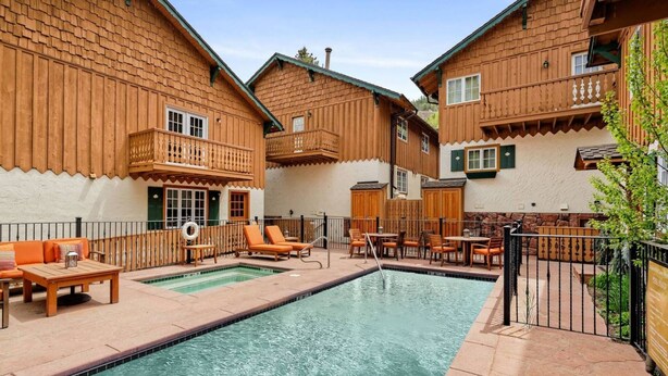 A pool area with wooden buildings, outdoor seating, and a clear sky. - One Block to Aspen Mtn, Dining, Shops & Nightlife. AC In Bedroom! W/D, Gas FP, Pool, HT, Parking (Aspen)