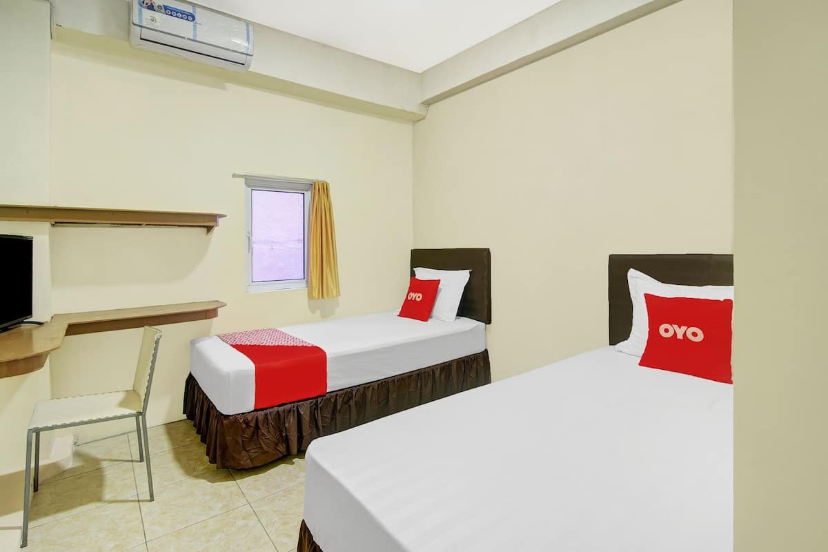 A hotel room with two beds, a desk, a chair, and a window with curtains.