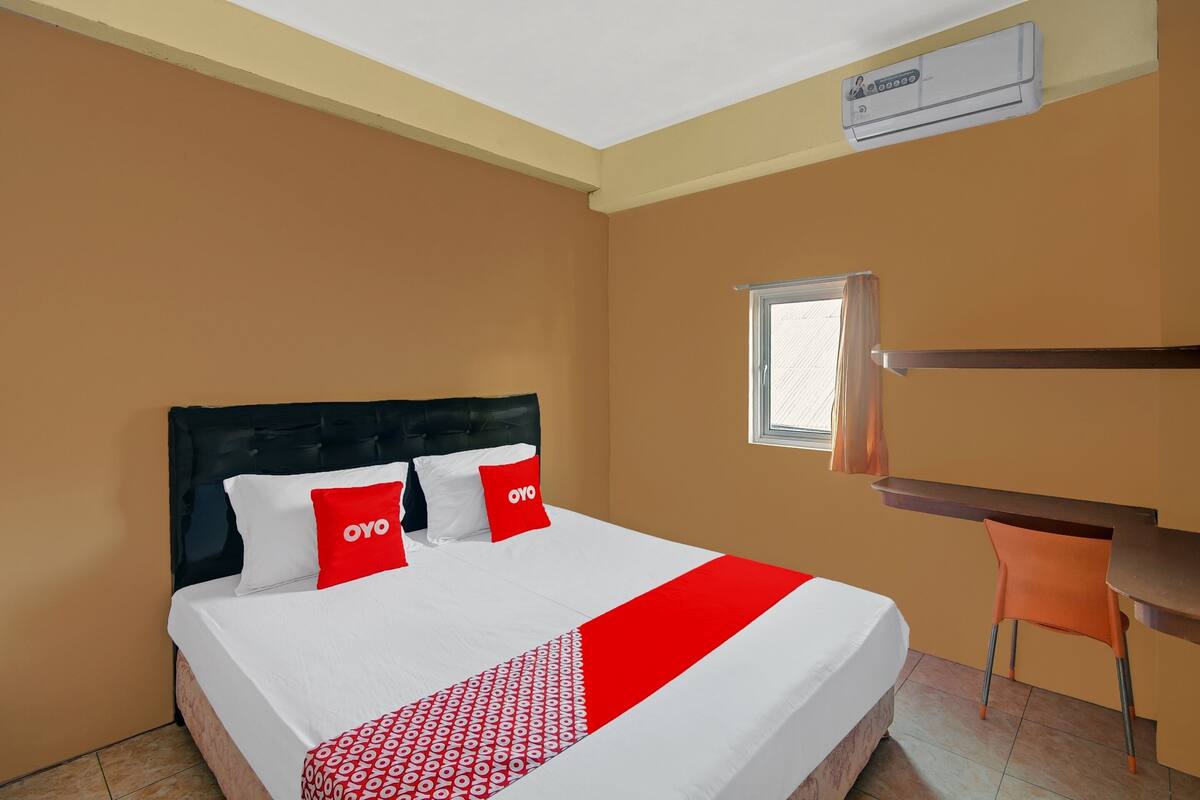 A hotel room with a bed, a desk, and an air conditioning unit.