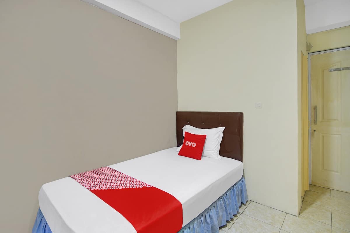A single bed with a white and red bedspread, a brown headboard, and a red pillow with "OYO" text.