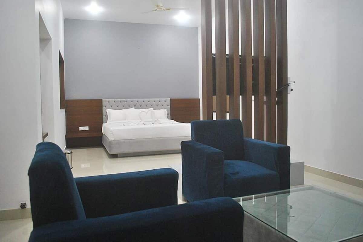 A bedroom with a bed, two blue armchairs, a glass coffee table, and a wooden partition.