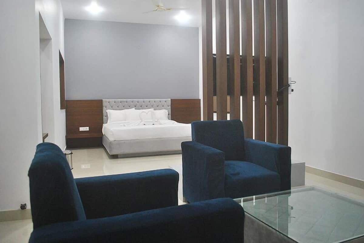 A bedroom with a bed, two blue armchairs, a glass coffee table, and a wooden partition.