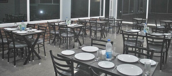A restaurant with multiple tables and chairs, arranged in a spacious outdoor setting with large windows.