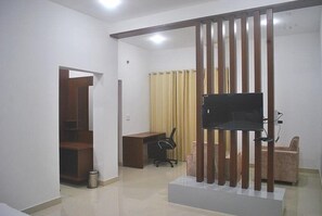 A modern living room with a flat-screen TV mounted on a wooden stand, a desk with a chair, and a sofa. - Himalayan Off Trails (Dharamshala)