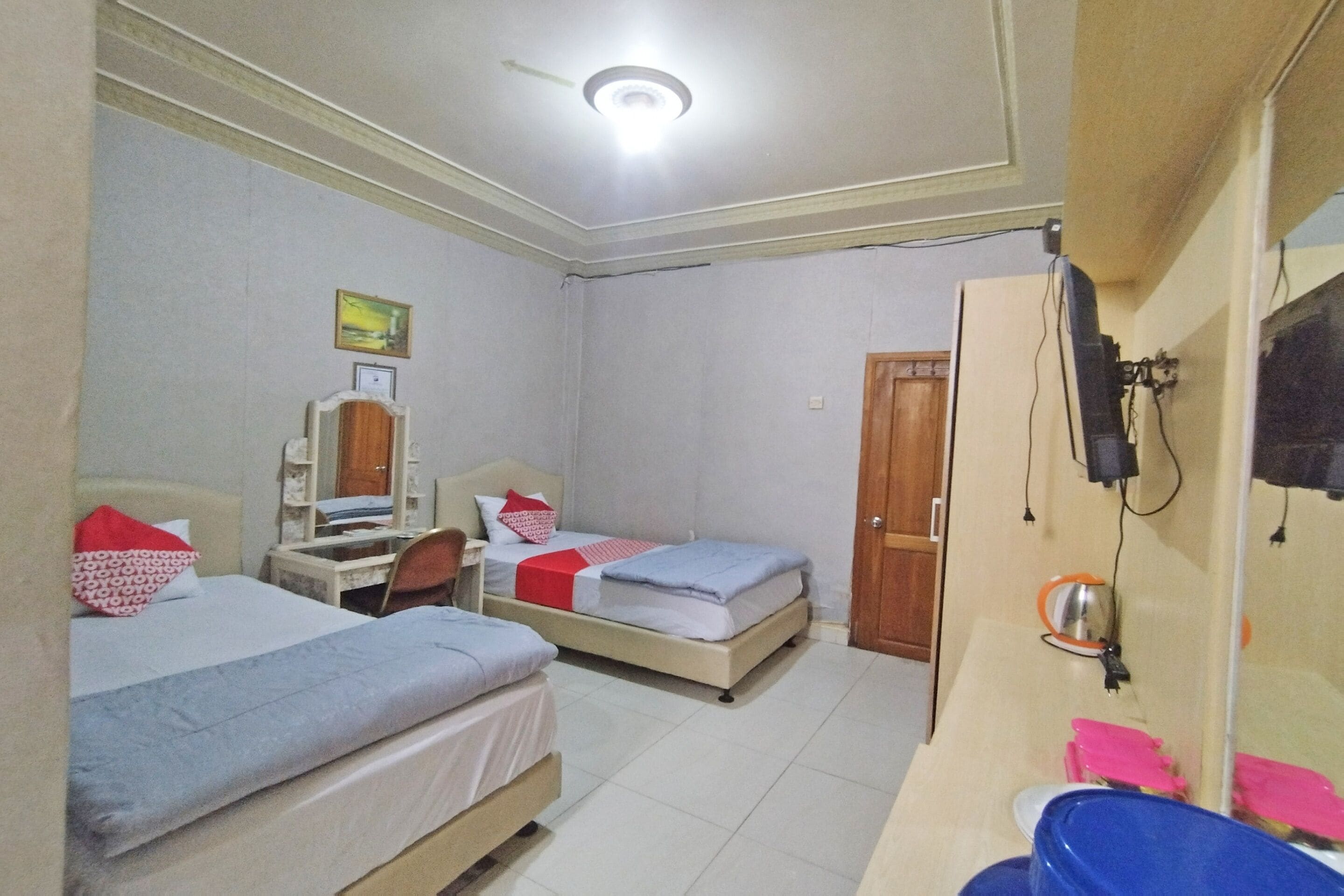 A bedroom with two beds, a desk, a chair, a mirror, and a bathroom with a sink and a toilet.
