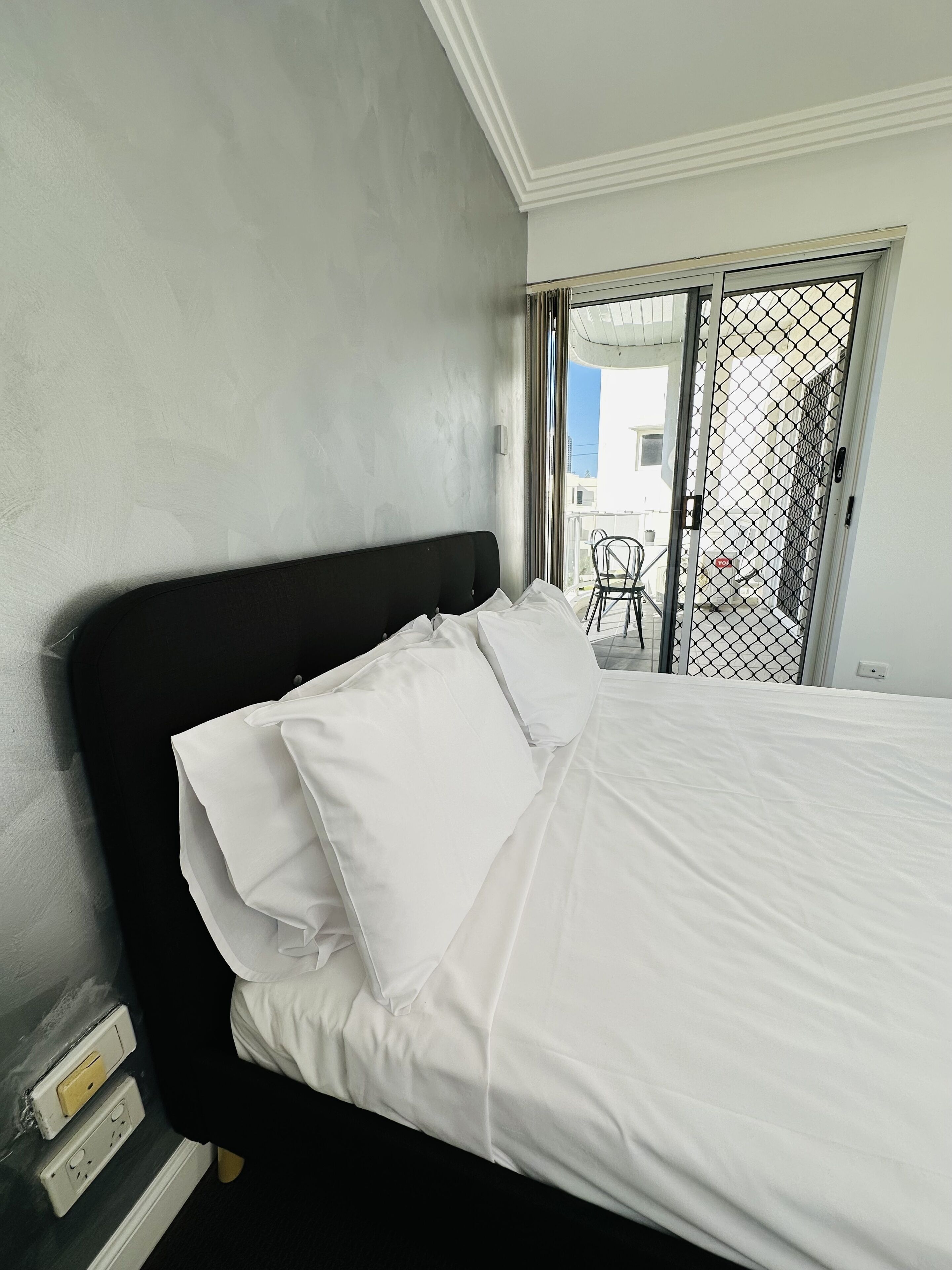 Un lit avec du linge de lit blanc, dans une pièce dont un mur est gris et qui possède une tête de lit noire.