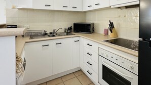 A modern kitchen with white cabinets, a microwave, a stove, and a sink. - Modern Apartment in Chevron Island (Surfers Paradise)