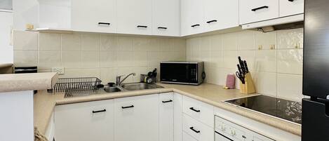 A modern kitchen with white cabinets, a microwave, a stove, and a sink.