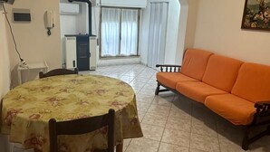 A dining area with a table and chairs, an orange sofa, and a kitchen in the background.