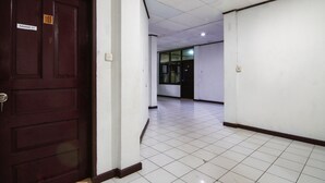 Un couloir avec une porte en bois sombre portant le numéro « 103 » et un sol carrelé de carreaux blancs.