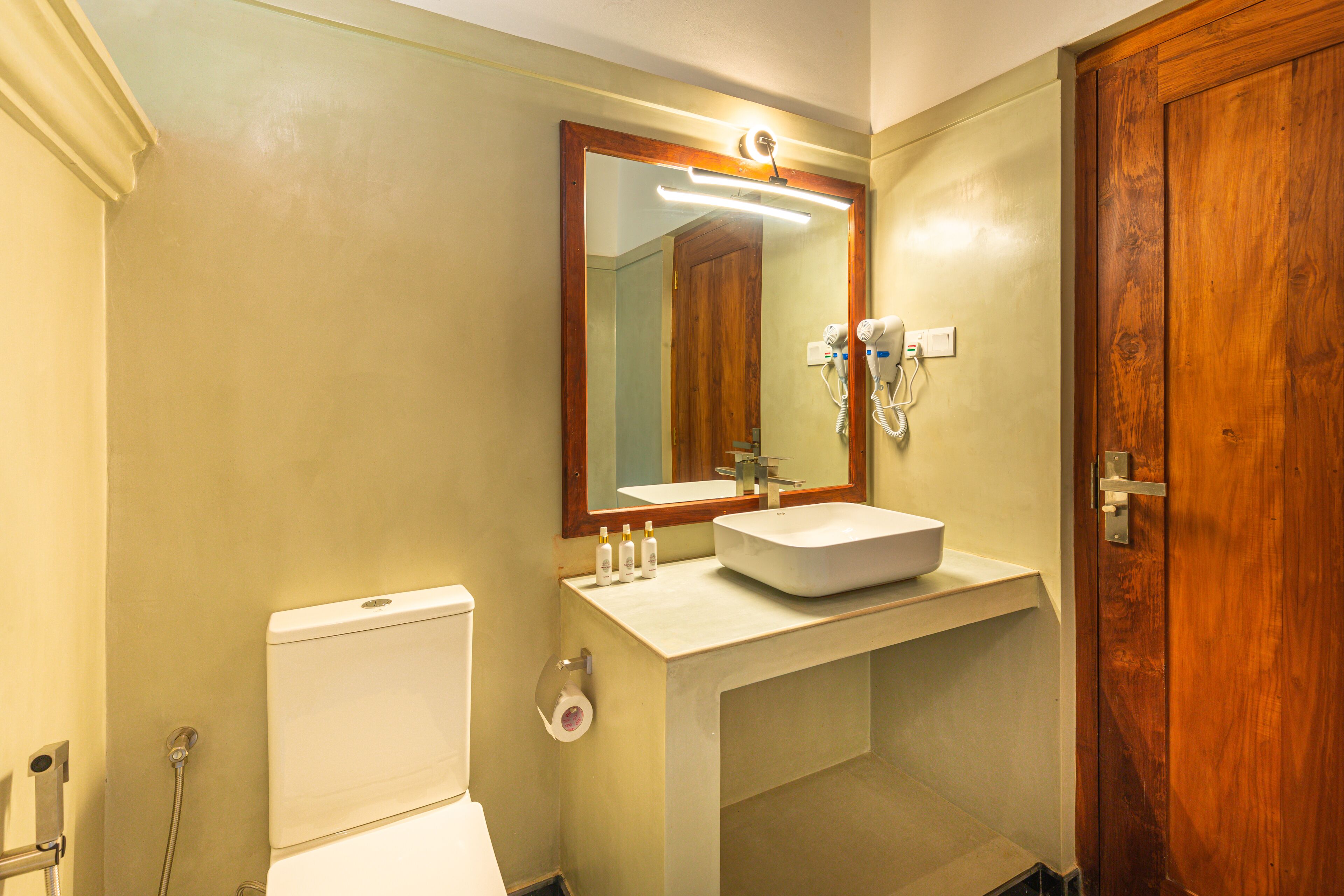 A bathroom with a toilet, sink, mirror, and wooden door.