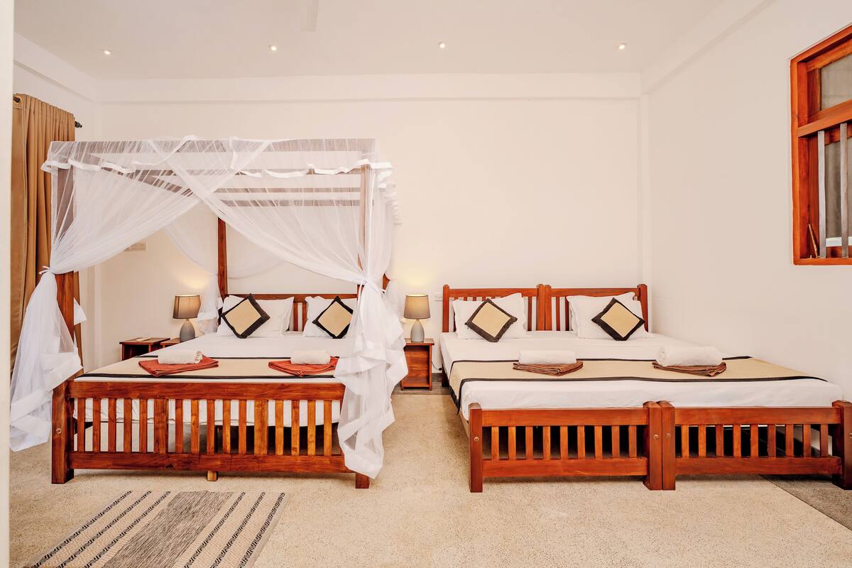 A hotel room with two wooden beds, each with a canopy bed, white bedding, and bedside tables with lamps.