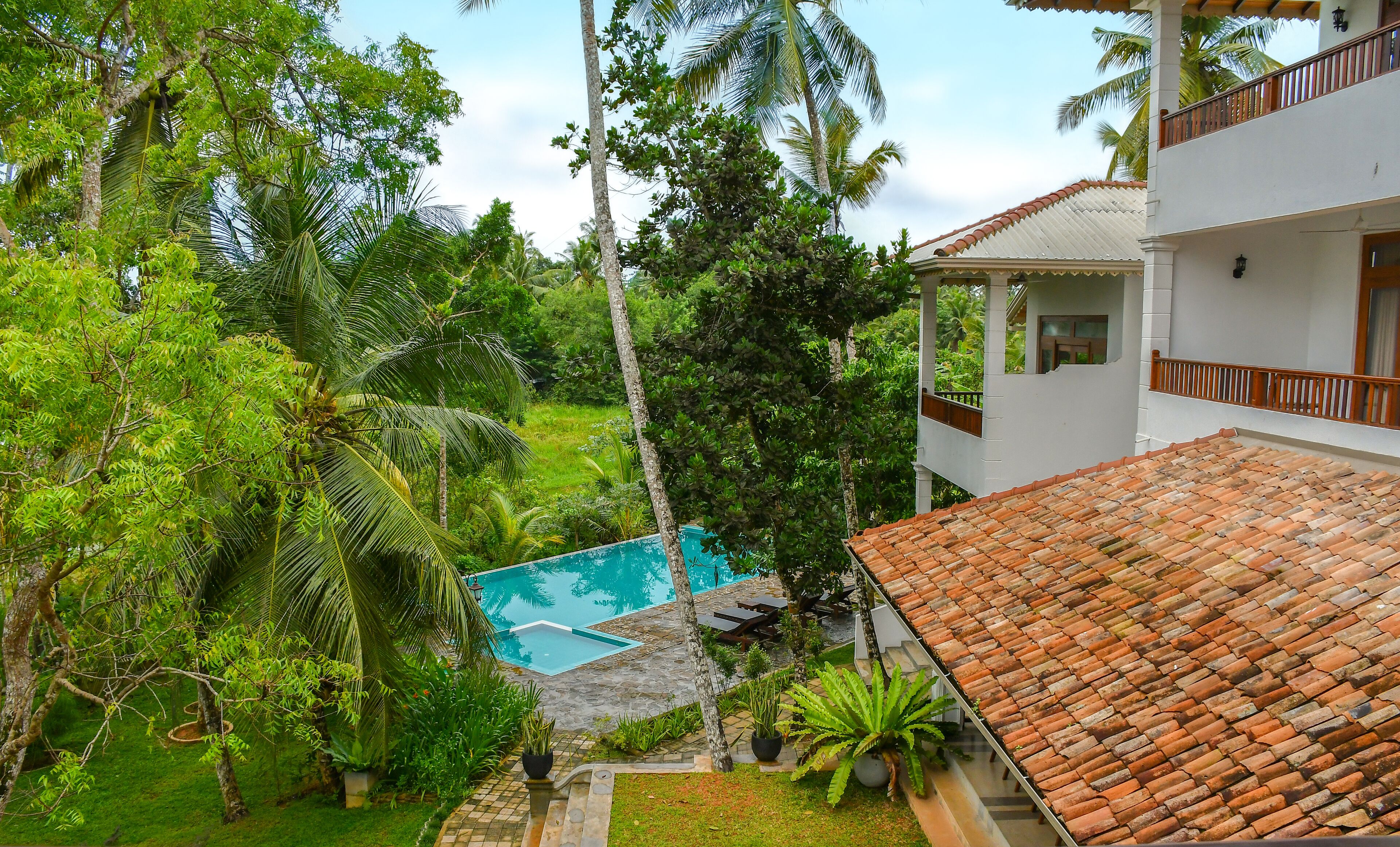 A villa with a tiled roof, a swimming pool, and lush greenery.