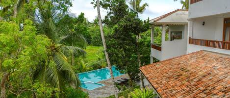 A villa with a tiled roof, a swimming pool, and lush greenery.