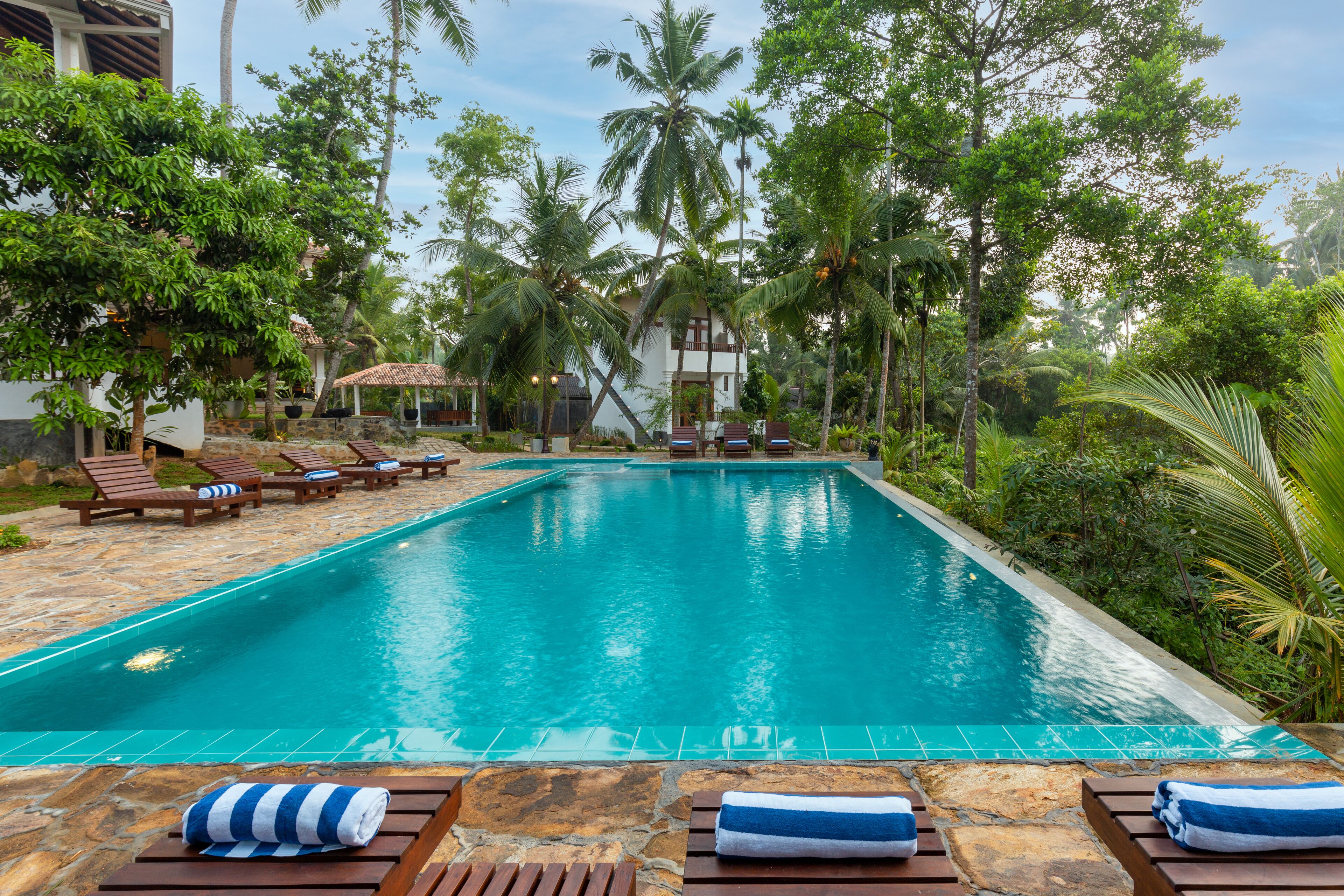 A swimming pool with lounge chairs and towels, surrounded by tropical vegetation and a stone deck.