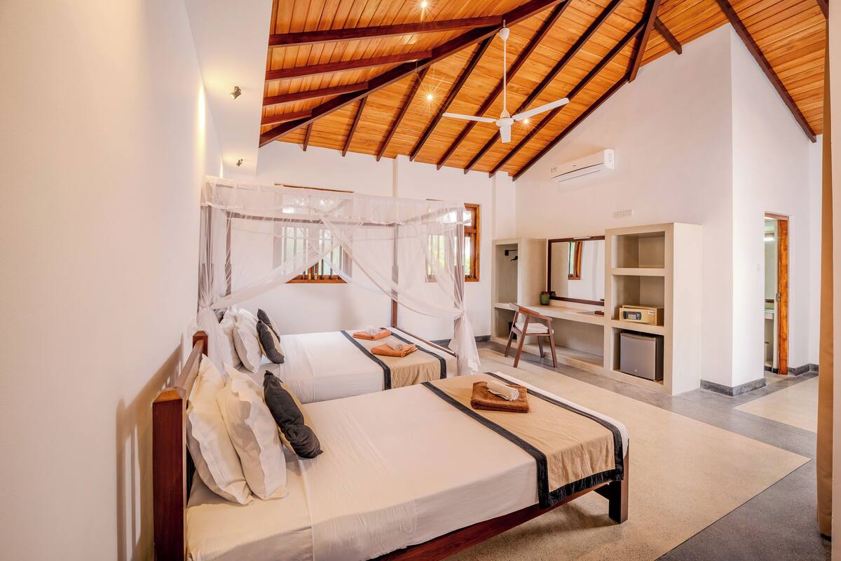 A four-poster bed with a canopy, a desk with a chair, and a small kitchenette in a hotel room.