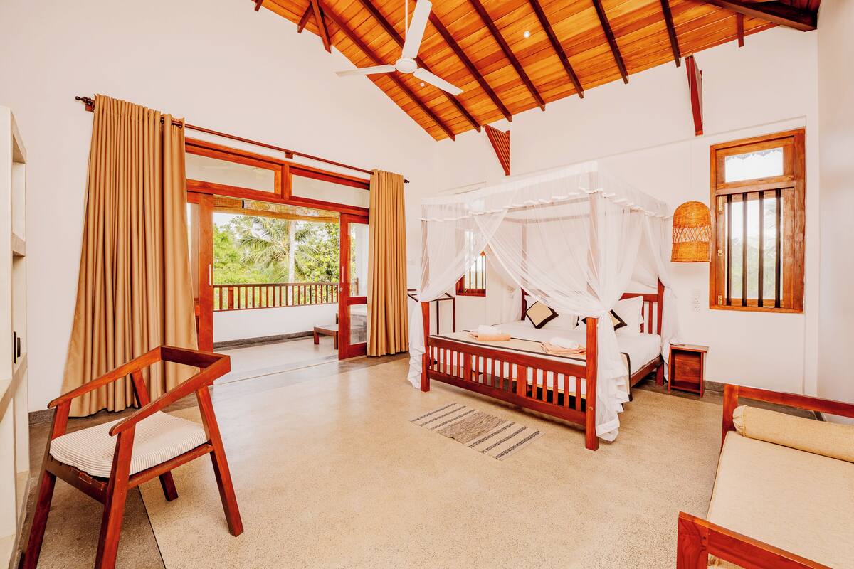 A bedroom with a wooden bed, a chair, a bedside table, a window with curtains, and a ceiling fan.