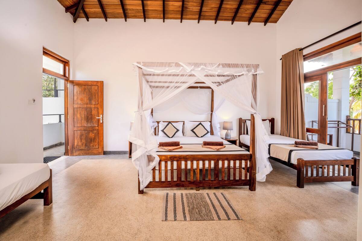 A bedroom with a four-poster bed, a wooden door, a small table, and a bench.