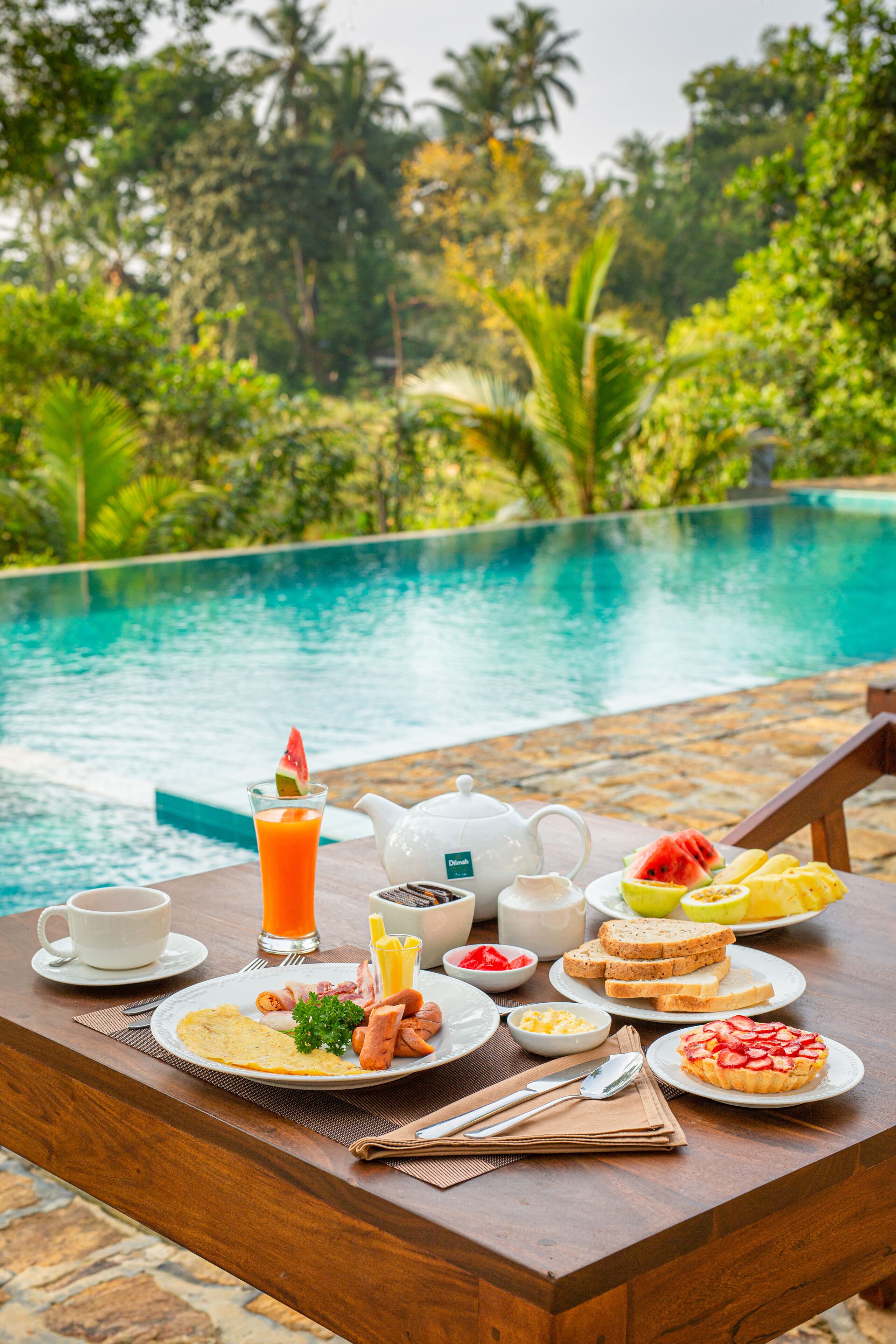 Una mesa de desayuno con diversos alimentos y un hervidor de agua junto a una piscina.