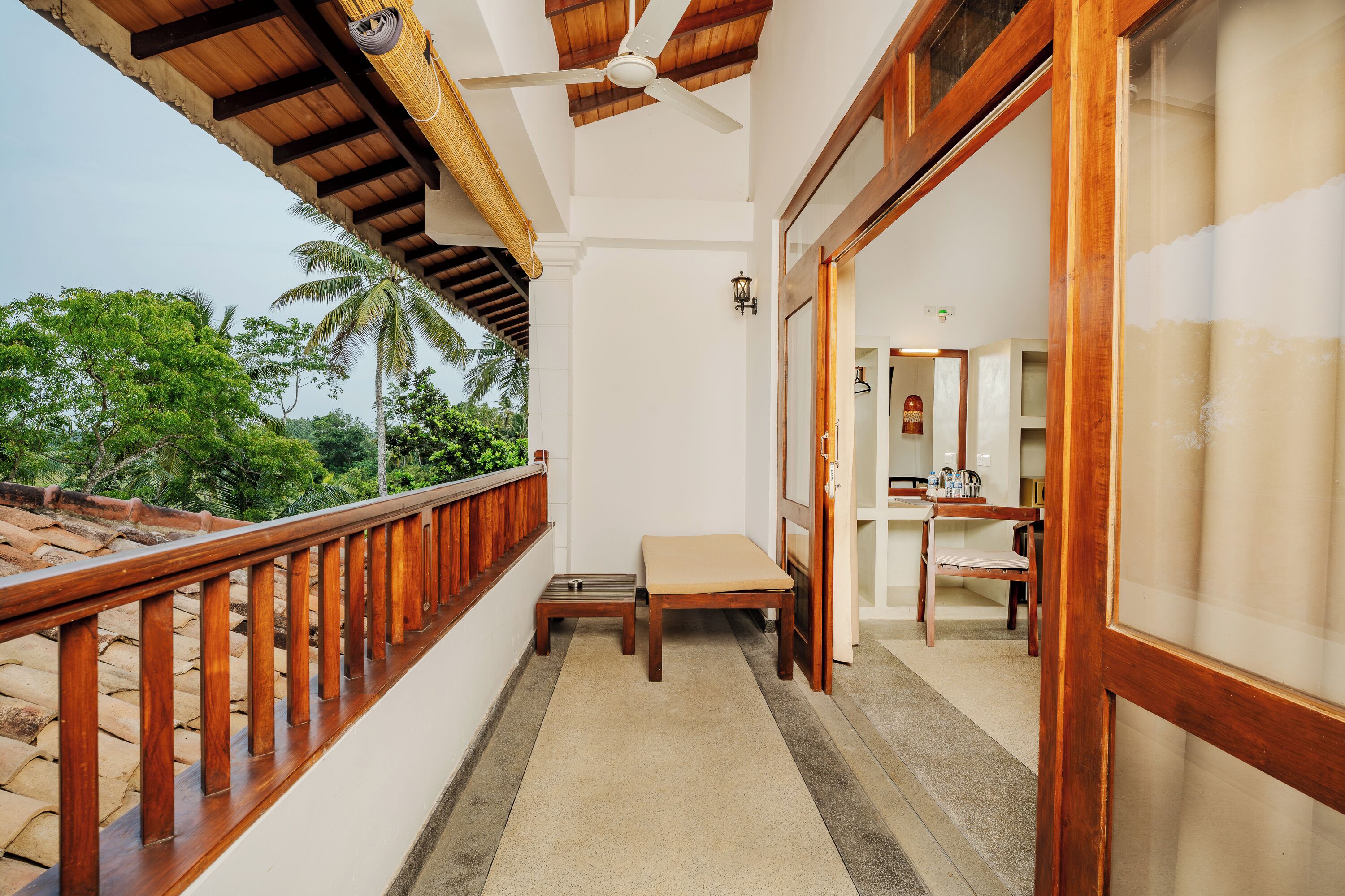 A balcony with a wooden railing, a ceiling fan, a small table, and a bench.