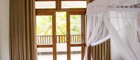 Una habitación con cama, cortinas y vista a palmeras a través de una puerta de vidrio.
