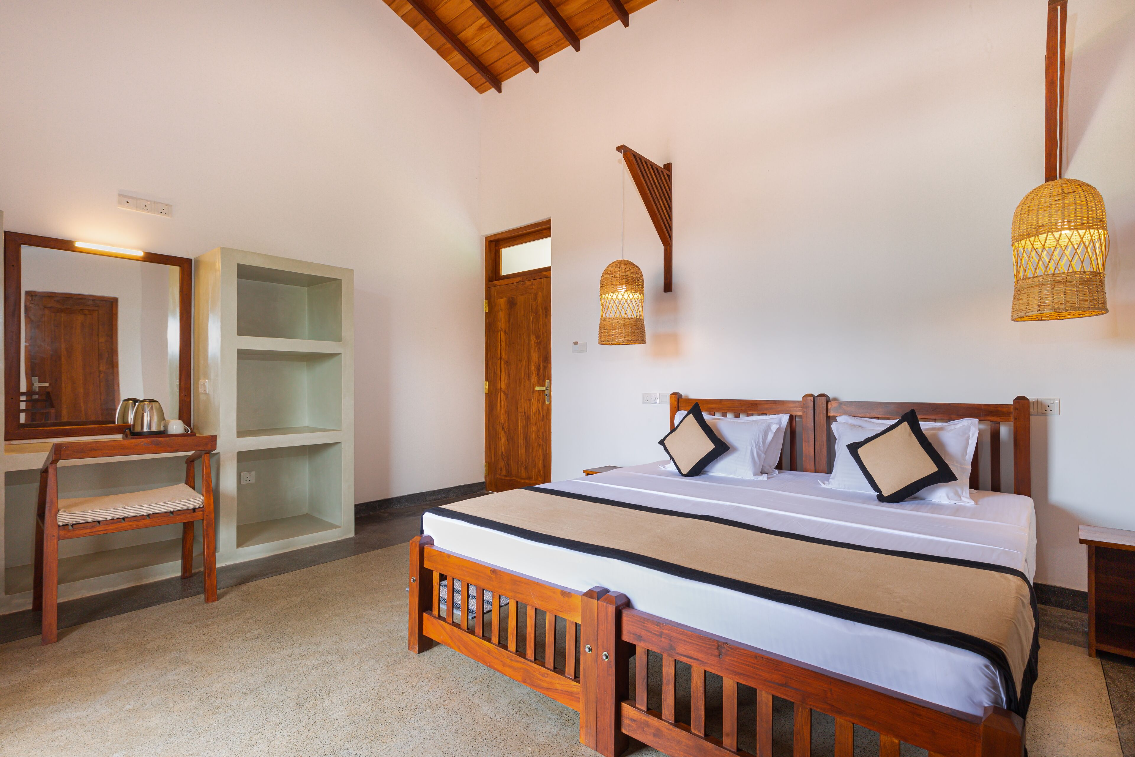 A bedroom with a wooden bed, a desk, and a chair. There is a door and a shelf unit in the background.
