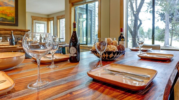 A dining table set with wine glasses, plates, and a bottle of wine. - Incredible Sunriver Retreat, Pet Friendly, Next to Pool and Golf Course, Hot Tub, BBQ (Sunriver)
