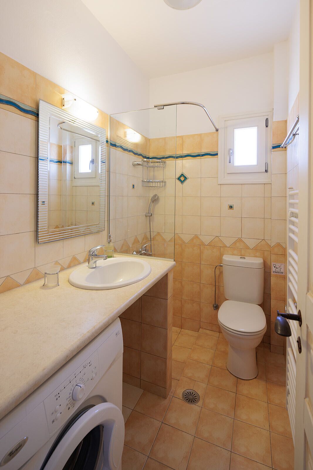 A compact bathroom with a sink, mirror, toilet, and a washing machine.